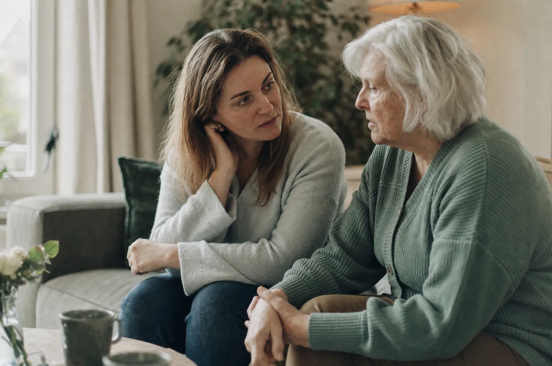 Zorgverlener met een arm om een oudere vrouw op de bank